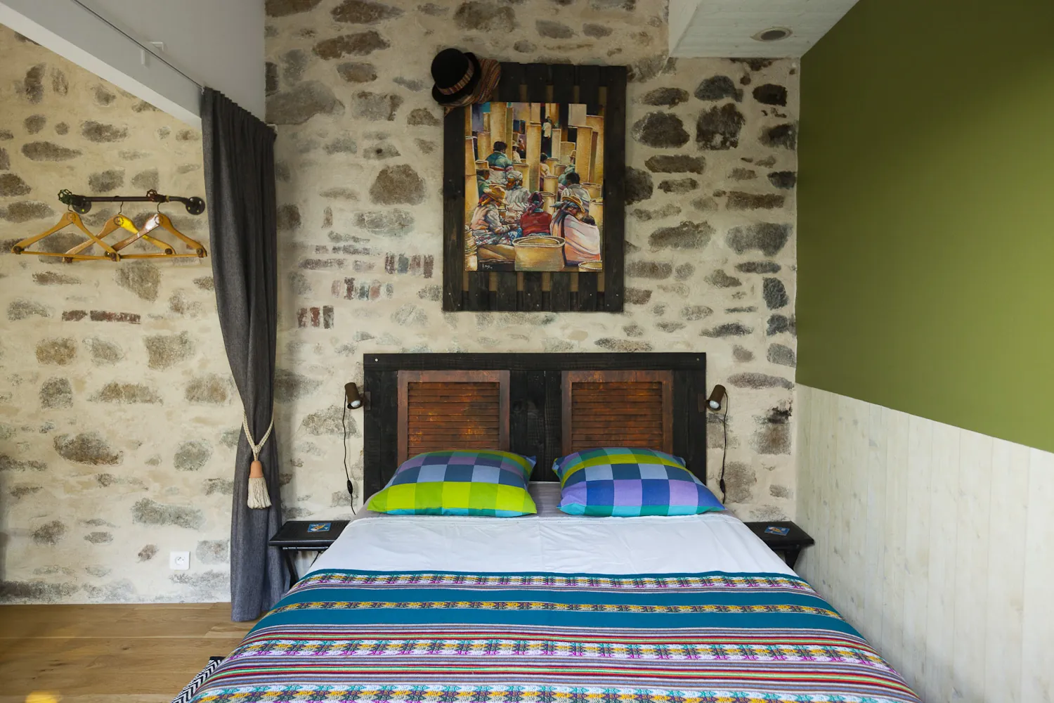 Chambre avec mur en pierre apparente, couettes colorées et tableau