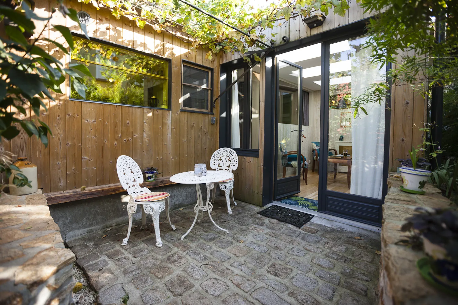 Terrasse en pierre avec table et chaises blanches sous tonnelles de vignes